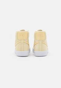 Gula högstövlar med en slät mocka yta, vit gummisula och präglad Nike-logga på baksidan.