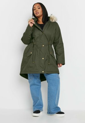 Khaki parka-jakke med hætte foret med pels, snoretræk i taljen, guldfarvede knapper, forlommer og en længere bagkant.