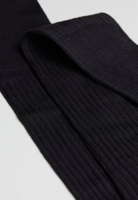 Tights negras con canalé que presentan una textura suave. La tela tiene un patrón uniforme con un ligero brillo, dobladas para mostrar su longitud y forma.