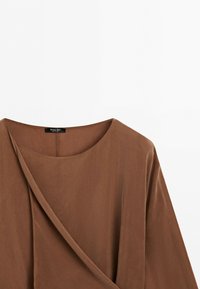 Brown long-sleeve blouse with round neckline and overlapping front panel detail against white background.