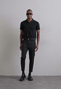 Cămașă polo neagră, pantaloni negri croiți și pantofi negri. Design minimalist, textură netedă, siluetă ajustată și fără modele vizibile.