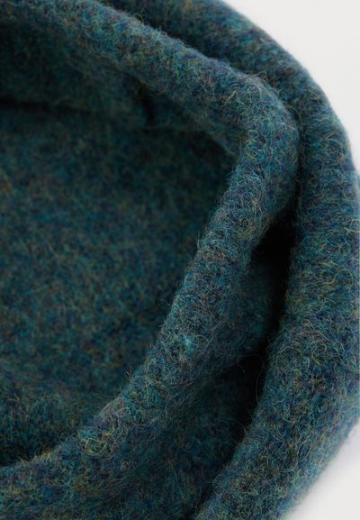 Υφασμα από μάλλινο σε σκούρο πράσινο-μπλε χρώμα με πιο ανοιχτές πιτσιλιές, που διαθέτει μαλακή, υφή αίσθηση και κυλινδρικό σχήμα, υποδηλώνοντας ζεστασιά και άνεση.