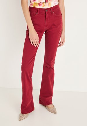 Jeans acampanados rojos hechos de algodón suave. Presentan un diseño clásico de cinco bolsillos y un cierre de botón metálico. Combinados con una blusa multicolor.