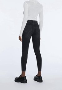 Černé skinny džíny s vysokým pasem, pětipocketovým designem a hladkou texturou, doplněné o robustní černé platformové boty.