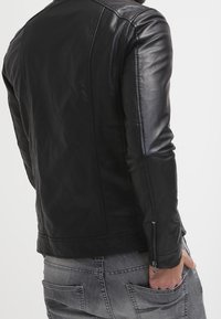 Černá kožená bunda s hladkou texturou, přiléhavým střihem a zipovými manžetami. Má jednoduchý design bez viditelných vzorů nebo akcentů.