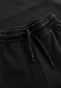 Pantalones jogger negros con cintura elástica y cordón. El material parece suave con una textura lisa. Diseño minimalista.