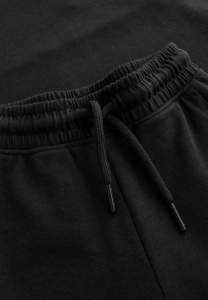 Schwarze Jogginghosen zum Hineinschlüpfen mit elastischem Bund und Kordelzug. Das Material wirkt weich mit einer glatten Textur. Minimalistisches Design.