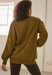 Oliven grøn sweatshirt med en afslappet pasform, ribbede manchetter og kant. Blød stoftekstur synlig, båret med sorte leggings. Bagudblik, uden mønstre.