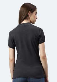 Schwarzes Polohemd mit kurzen Ärmeln, glatter Textur und klassischem Kragen, von hinten betrachtet. Minimalistisches Design, kein sichtbares Logo.