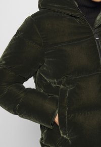 Zateplená bunda z tmavozeleného sametu s kapucí, s zipovým uzavíráním, bočními kapsami a jemnou, hladkou texturou.