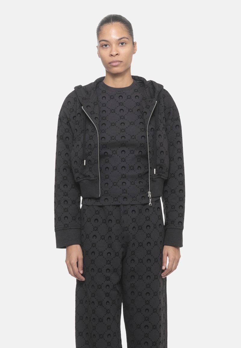 Felpa nera cropped con chiusura a zip, caratterizzata da un motivo testurizzato. Abbinata a pantaloni coordinati, realizzati in un materiale morbido e liscio.