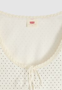 Top Levi's ivoire à petits pois noirs, bordure festonnée à l'encolure, détail noué à l'avant et étiquette taille small à l'intérieur du col.