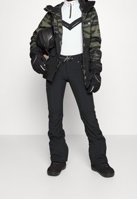 Snowboardutrustning med en grön kamouflagemönstrad jacka, vit zip-up-tröja, svarta byxor och handskar, samt en svart hjälm i handen.