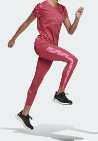 Rosa Sportoutfit, bestehend aus einem T-Shirt mit kurzen Ärmeln und Logo sowie gemusterten Schulterakzenten, kombiniert mit enganliegenden Leggings im geometrischen Design.