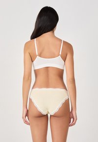 Bralette blanche avec fines bretelles et culotte à carreaux jaunes avec dentelle sur les bords, mettant en valeur une texture de tissu lisse et doux.