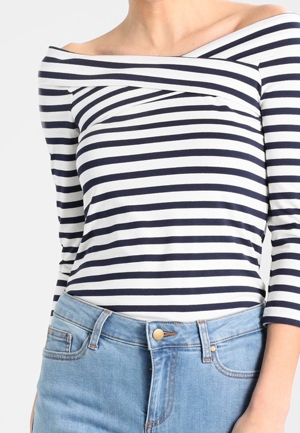 Granatowa i biała bluzka z długim rękawem w paski, z dekoltem bez ramion, wykonana z miękkiego materiału, zestawiona z jasnoniebieskimi spodniami z wysokim stanem.