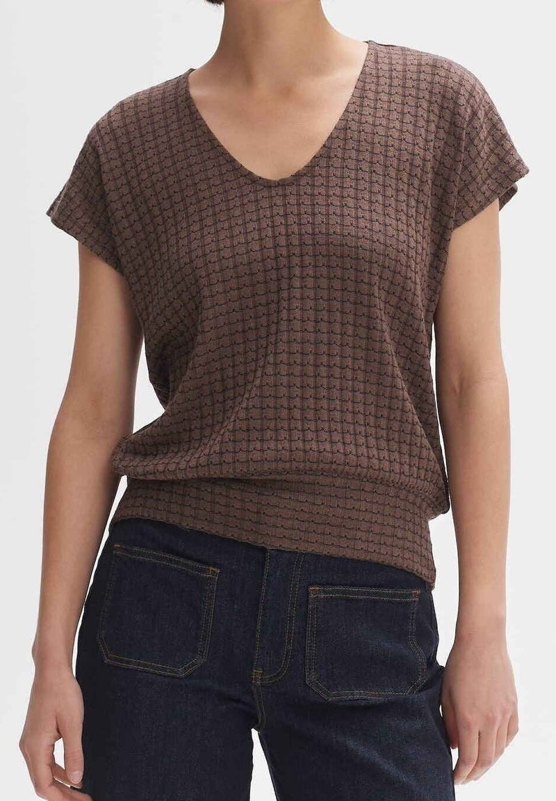 Top marrón de manga corta con escote en V y un patrón texturizado en forma de cuadrícula. Combina con unos vaqueros de denim azul oscuro con bolsillos traseros.