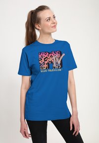 Camiseta azul de manga corta con un logotipo de MTV en estampado de leopardo en rosa y negro, con el texto "MUSIC TELEVISION" en dorado debajo del logotipo.