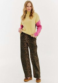 Pletený sveter v žltej farbe s ružovými rukávmi, skombinovaný s voľnými nohavicami s leopardím vzorom a hnedými platformovými topánkami so remienkami.