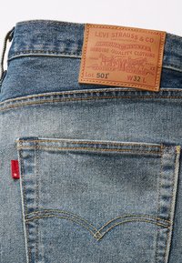 Jeans Levi's 501 in denim blu chiaro. Presentano una patta in pelle in vita, cuciture arancioni e la caratteristica etichetta rossa sulla tasca.