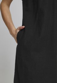 Abito in lino nero con vestibilità morbida, dotato di tasche laterali e una texture liscia. Il design presenta linee pulite e dettagli minimi.