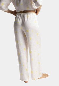 Pantalon de pyjama blanc avec imprimé floral jaune, taille élastique, coupe ample et tissu léger. Texture douce et design à jambe droite.