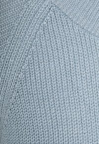 Close-up of light blue knitted fabric with varied stitch patterns and ribbed seam detail.