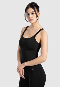 Top sportivo nero senza maniche con spalline sottili, scollatura rotonda e siluetta aderente. Tessuto liscio con dettagli di branding minimi.
