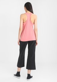 Top di cotone rosa senza maniche con design racerback, abbinato a pantaloni neri a gamba larga e scarpe di tela nere. Aspetto pulito e minimalista.