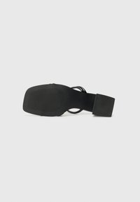 Black sandals with a flat sole, featuring a textured footbed and a wide ankle strap. The design includes a square heel and minimalist accents.