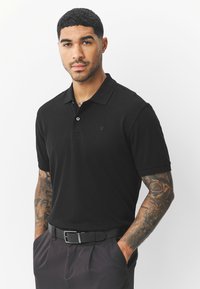 Mustast, siledast kangast poloõlg, millel on krae ja kaks nööpi ning rindkerel peen logo. Kandmisel tumedad püksid ja must vöö.