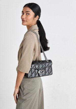 Bolsa de ombro preta em couro acolchoado com alça em corrente prateada e tachas decorativas, apresentando um fecho com logotipo na frente.