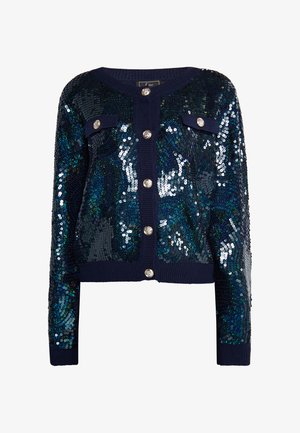 Tamsiai mėlynas blizgantis megztinis su sidabriniais mygtukais, turintis rauktą apykaklę ir rankogalius, bei dvi priekinės kišenės. Šviečiančio, tekstūruoto paviršiaus su raštais.