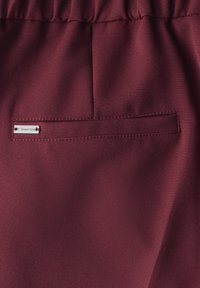 Tissu bordeaux avec une texture lisse comprenant une poche plate au dos. Une petite étiquette indiquant "Street One" est visible sur la poche.