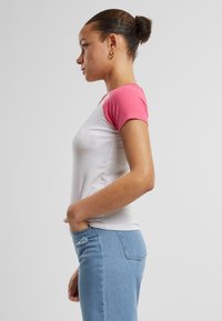 T-shirt blanche courte avec des manches courtes roses, coupe ajustée et tissu lisse ; associé à un jean en denim bleu clair avec des détails de couture subtils.