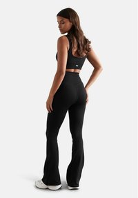 Schwarzes, geripptes Sport-Outfit mit einem kurzen Tanktop und hoch taillierten, ausgestellten Hosen, gefertigt aus elastischem Material für eine enge Passform.