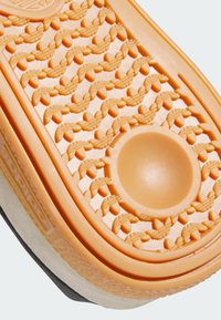 Potplat cipele u narančastoj gumi s teksturiranim, uzorkovanim dizajnom; sadrži kružnu udubinu i glatku ivicu u svijetlo sivoj boji.