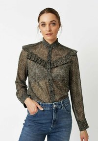Black and gold patterned blouse with ruffled collar, button front, and long sleeves, paired with blue denim jeans. Soft, textured fabric.
