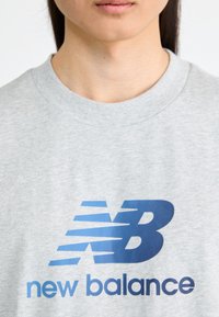 Gray cotton sweatshirt featuring a prominent blue "new balance" logo. The logo includes stylized stripes above the letter "B".
