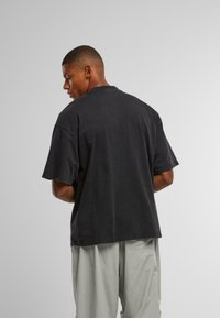Črna bombažna majica, oversize kroja s kratkimi rokavi in okroglim izrezom. Vidne šive okoli roba in ramen.