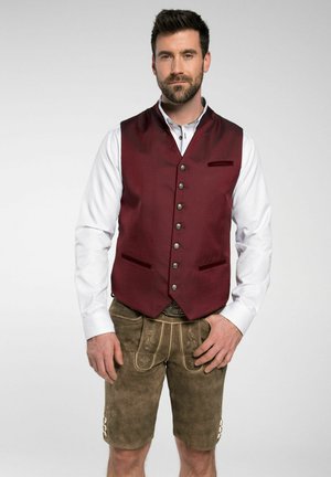 Bordeauxfarbener Weste aus strukturiertem Stoff mit silbernen Knöpfen, kombiniert mit braunen Lederhosen, die dekorative Nähte und Seitentaschen aufweisen.