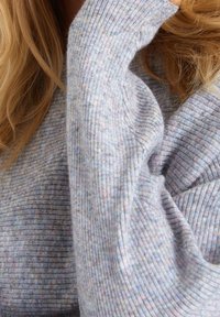 Pull en maille côtelée bleu clair avec de subtiles touches de couleur. Il présente des manches longues et un ajustement près des poignets. Tissu doux et texturé.