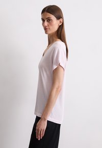Lichtroze T-shirt met korte mouwen en een V-halsontwerp, gemaakt van een zachte stof, met een relaxte snit en een gladde textuur.