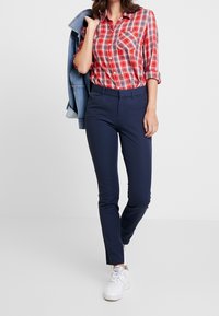 Chemise à carreaux rouges et bleus avec un devant boutonné et une poche poitrine, associée à un pantalon bleu marine slim et des baskets blanches, avec une veste en jean.