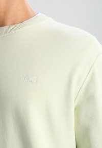 Sweat-shirt vert clair avec encolure ronde côtelée. Présente un logo "VANS" blanc brodé sur la poitrine. Texture douce, style décontracté.