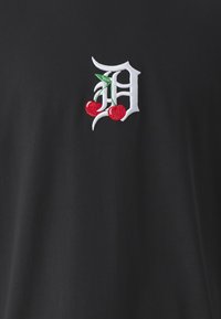 Camiseta negra con una letra "D" bordada en blanco, adornada con cerezas rojas y hojas verdes, hecha de material de algodón suave.