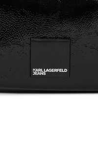 A fekete, textúrált anyagon egy téglalap alakú folt található, rajta fehér betűkkel a "KARL LAGERFELD JEANS" felirattal, az alján középen.