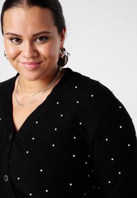 Zwarte cardigan met ronde parelaccenten, V-hals en knoopsluiting. Glad oppervlak met een aansluitend ontwerp.