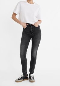 Jeans skinny de tiro alto en negro combinados con una camiseta corta blanca y zapatillas negras con detalles en gris. Textura de denim suave.
