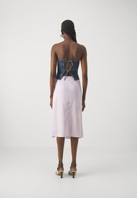 Denim bustier med åpen ryggdesign, sammen med en lys lilla, kne-lang skjørt. Har tynne stropper og en avslappet passform.
